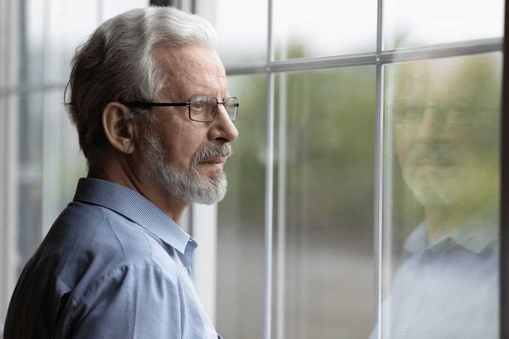 Elderly man gazing thoughtfully outside.